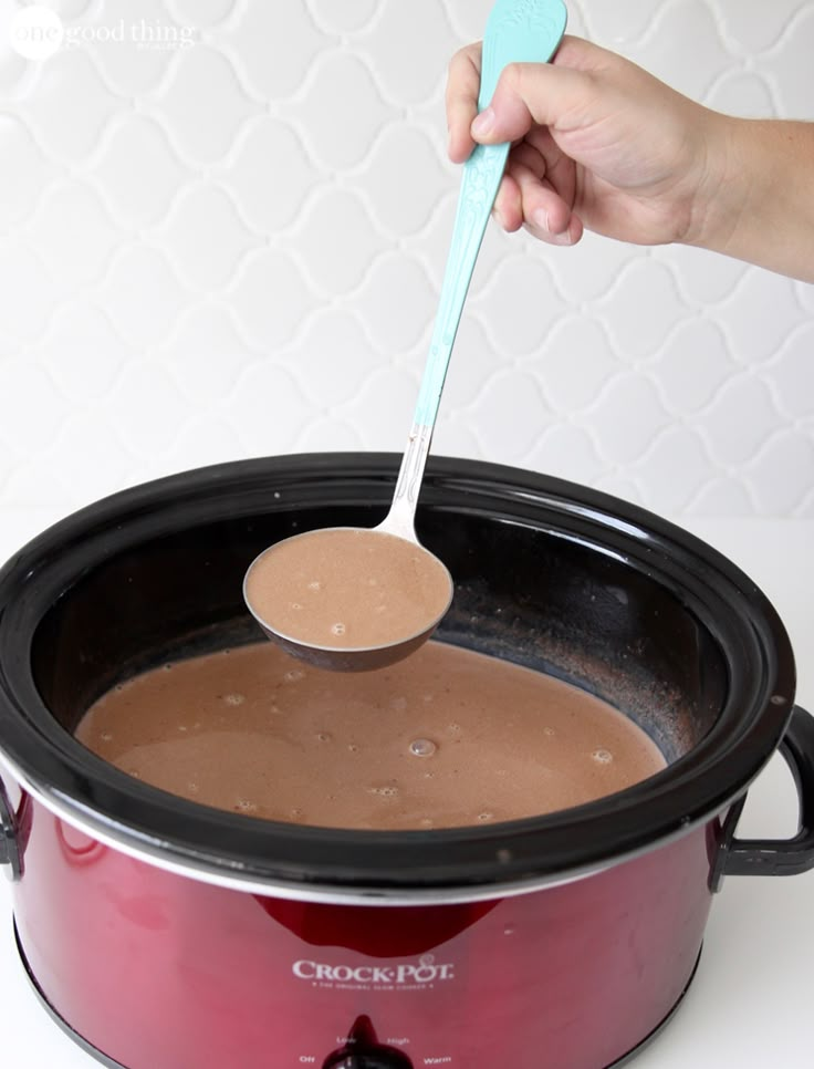 a person spooning chocolate into a crock pot with a plastic spoon in it