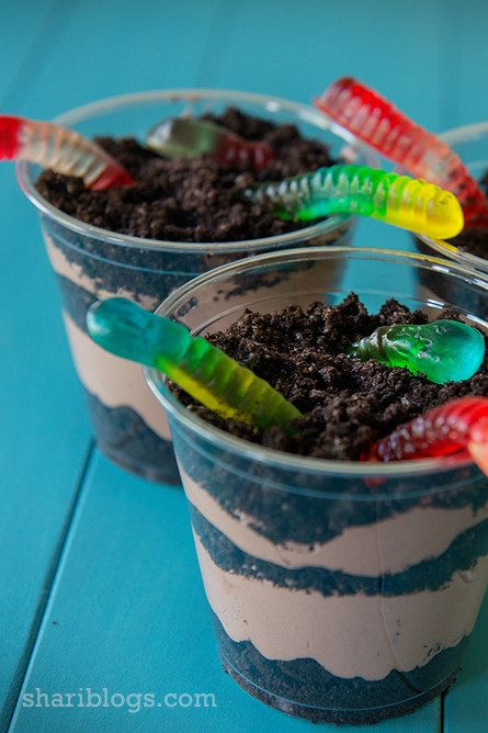 two plastic cups filled with dirt and toothbrushes sitting on top of a blue table