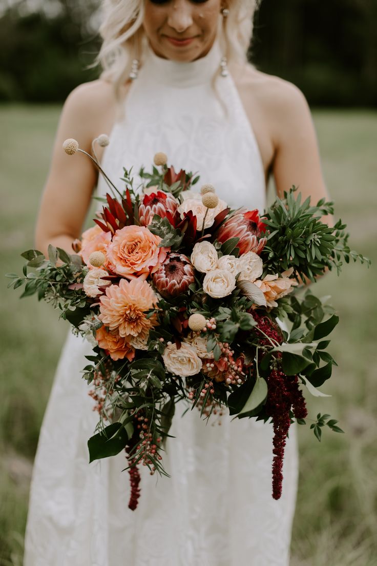 a woman in a white dress holding a bouquet of red and orange flowers on her wedding day