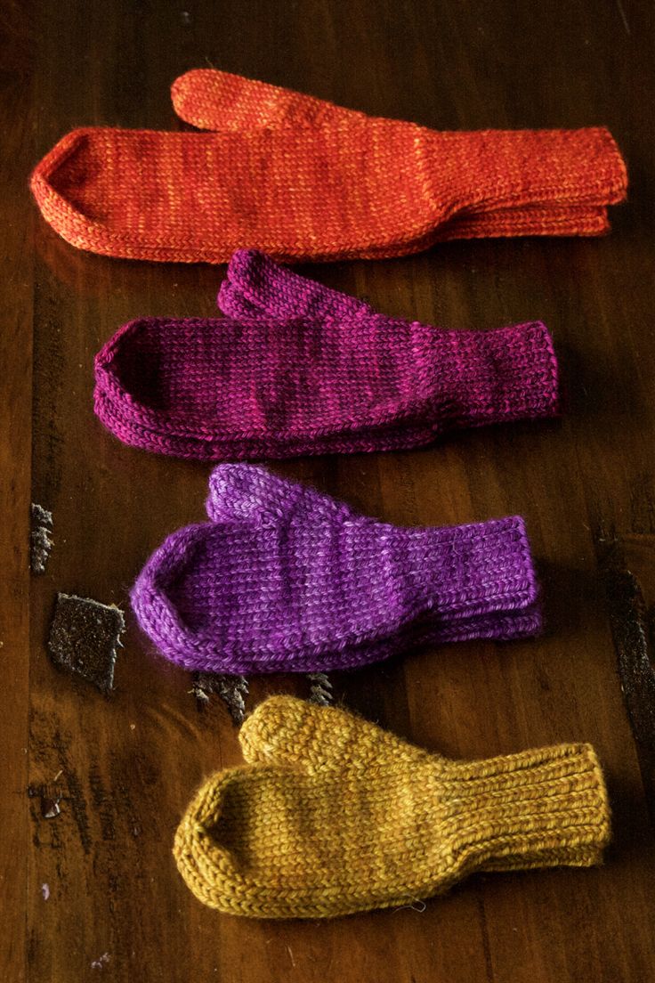 three knitted mittens sitting on top of a wooden table next to each other