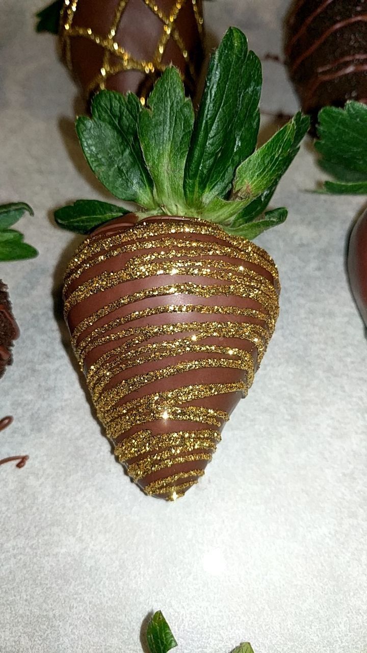 some chocolate covered strawberries are sitting on a table with green leaves and gold decorations