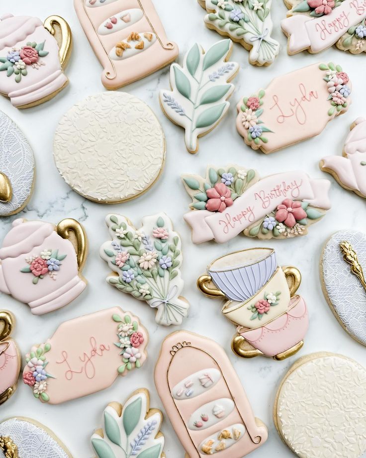 many decorated cookies are laying on the counter top, some with flowers and teapots