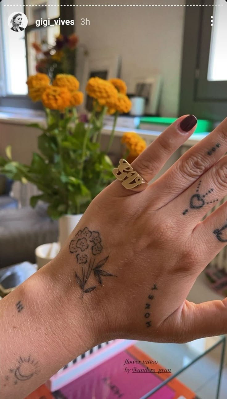 a woman's hand with tattoos on it and flowers in the vase behind her