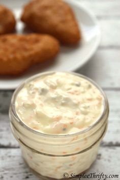 some food is in a small glass jar on a white plate and next to two fried chicken nuggets