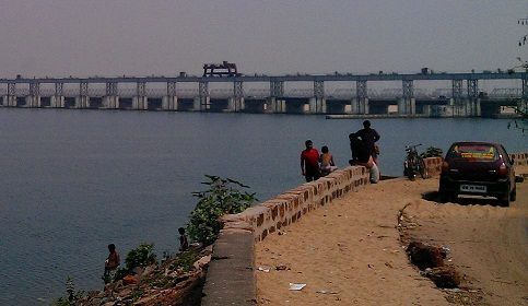 people standing on the edge of a beach next to a body of water with a bridge in the background