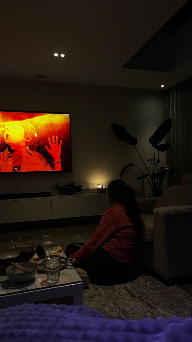 a woman sitting on the floor in front of a large screen tv with her hands up