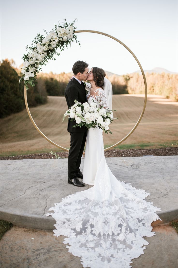 a bride and groom kissing in front of a circular arch with white flowers on it