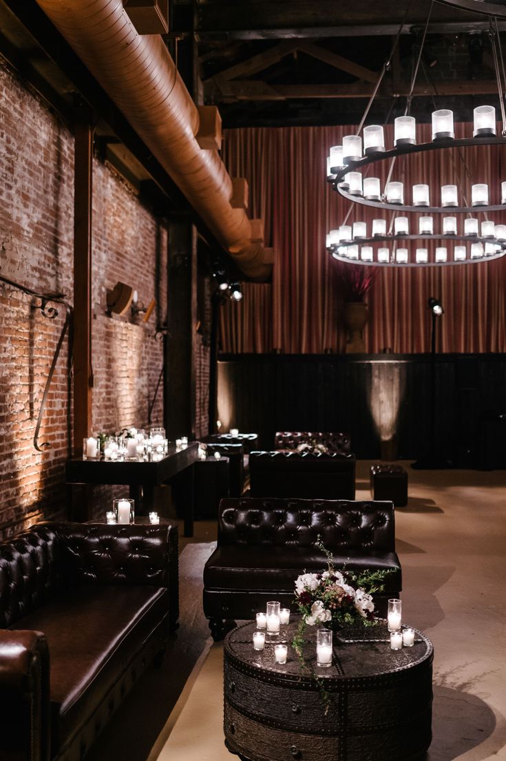 a dimly lit room with couches, tables and candles on the floor in front of a brick wall