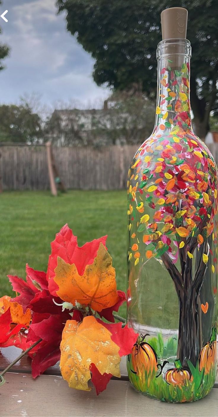 there is a glass bottle with leaves on it and flowers in the vase next to it