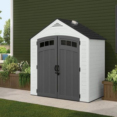 a white and gray shed sitting in front of a green house