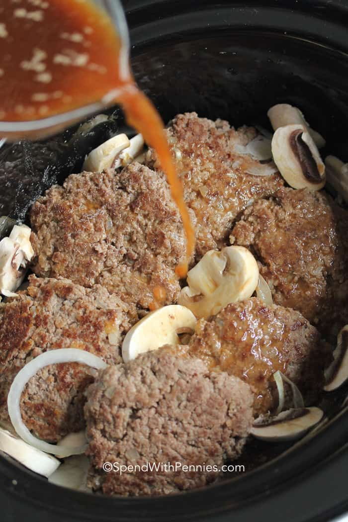 the meat is being poured into the slow cooker with onions and mushrooms in it