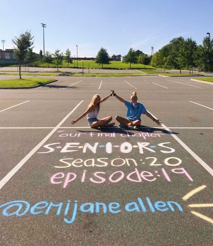 two people sitting in the middle of an empty parking lot with chalk writing on it