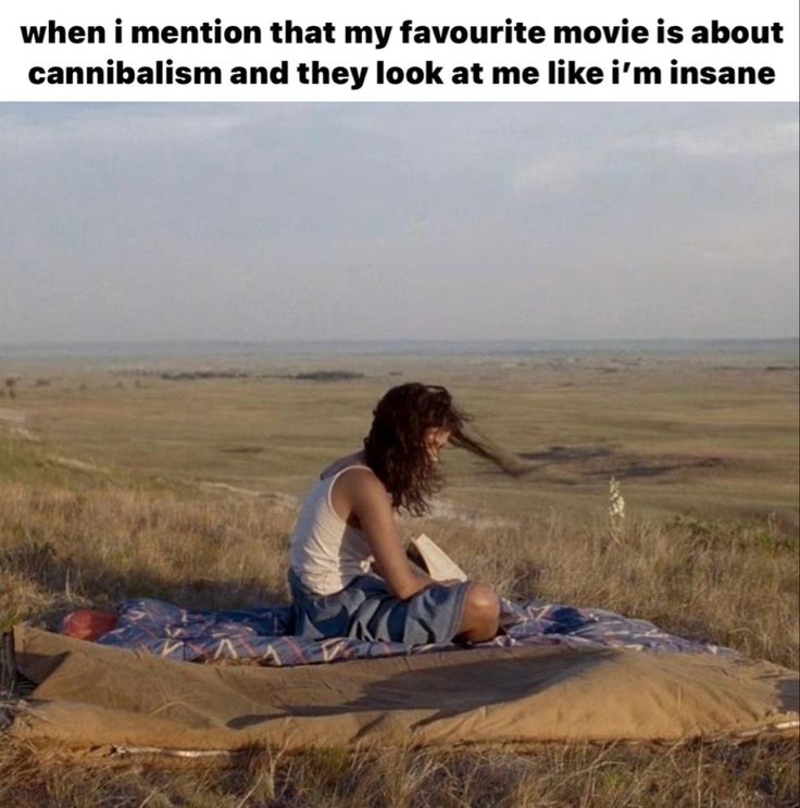 a woman sitting on top of a blanket in the middle of a field with her hair blowing