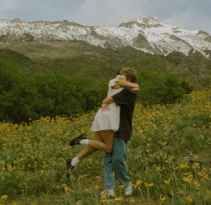 a man and woman hugging in a field with mountains in the background