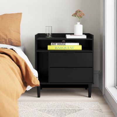 a nightstand with books on it next to a bed