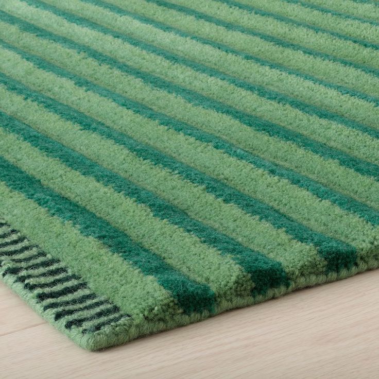 a green rug with vertical stripes on the top and bottom, sitting on a wooden floor