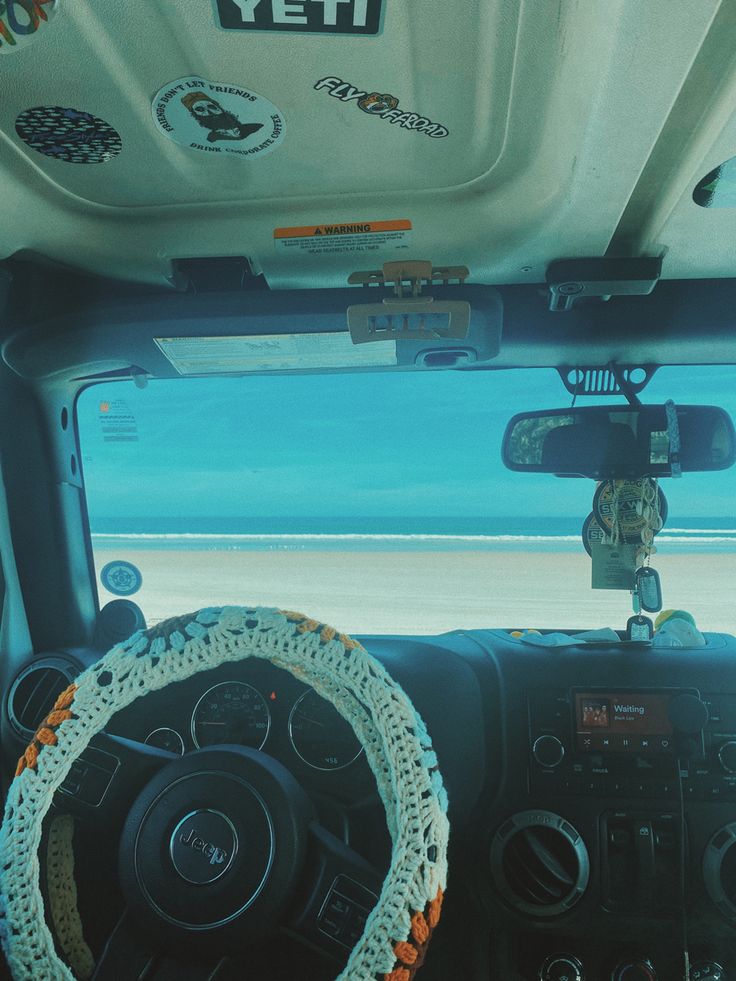 the interior of a vehicle with steering wheel and dash rope attached to the dashboard, looking out over an ocean