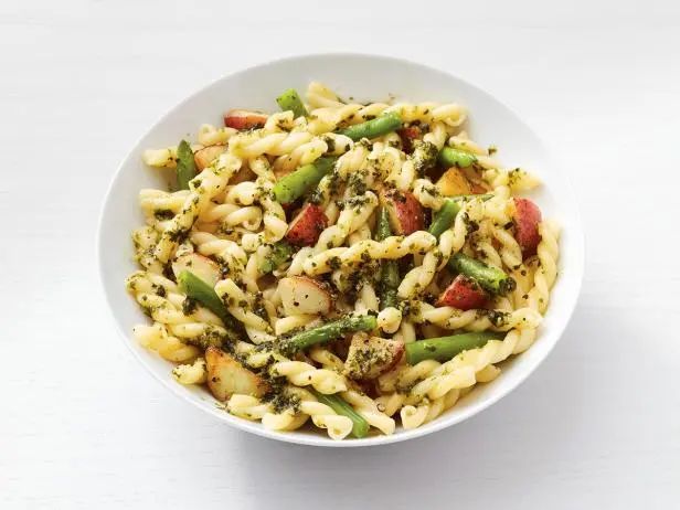 a bowl filled with pasta and vegetables on top of a white table next to a fork