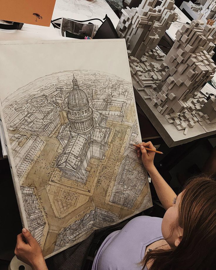 a woman is drawing on a piece of paper in front of some model city buildings