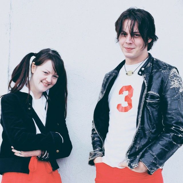 a young man and woman standing next to each other in front of a white wall