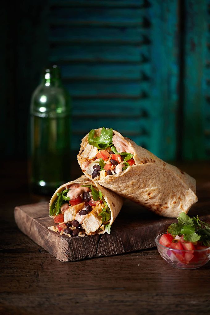 two burritos are sitting on a cutting board with tomatoes and lettuce