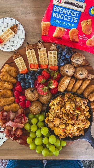 an assortment of breakfast foods are arranged on a wooden platter with waffles, grapes, strawberries and other snacks