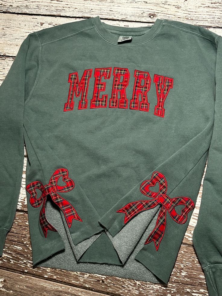 a green sweatshirt with red plaid bows and merry written on the front, sitting on a wooden surface