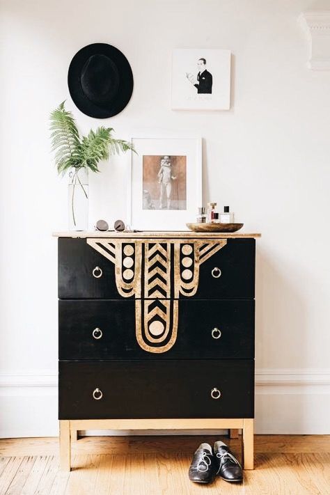 a black and gold chest of drawers in a white room with pictures on the wall