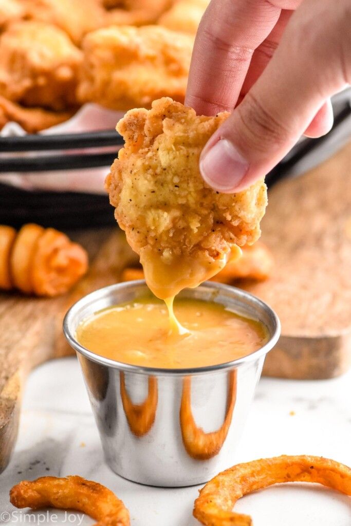 a person dipping some food into a small metal cup filled with sauce and pretzels in the background