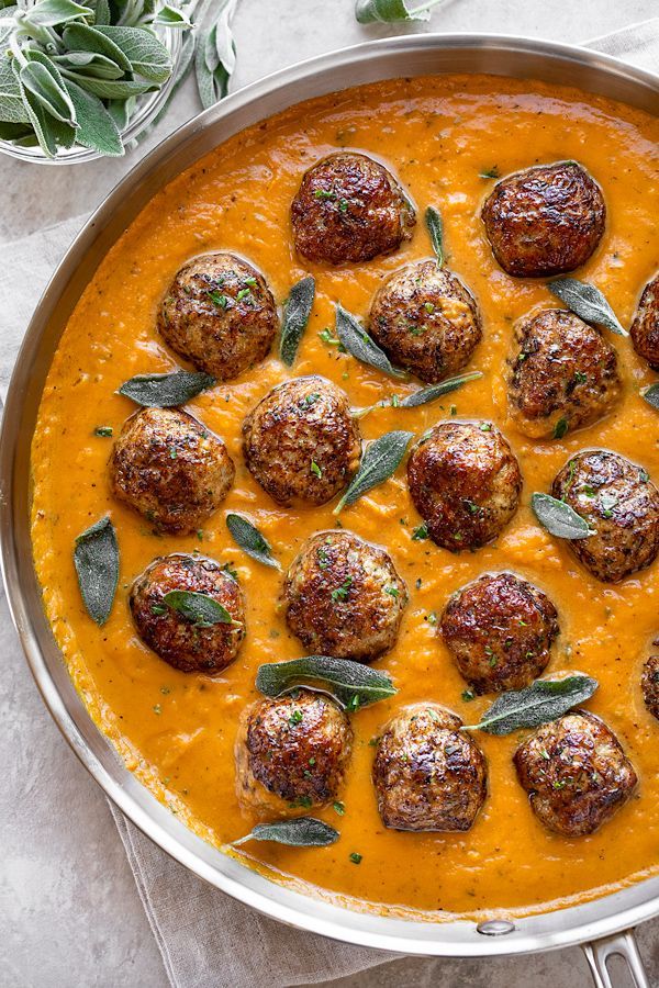 a pan filled with meatballs covered in sauce and garnished with sage leaves