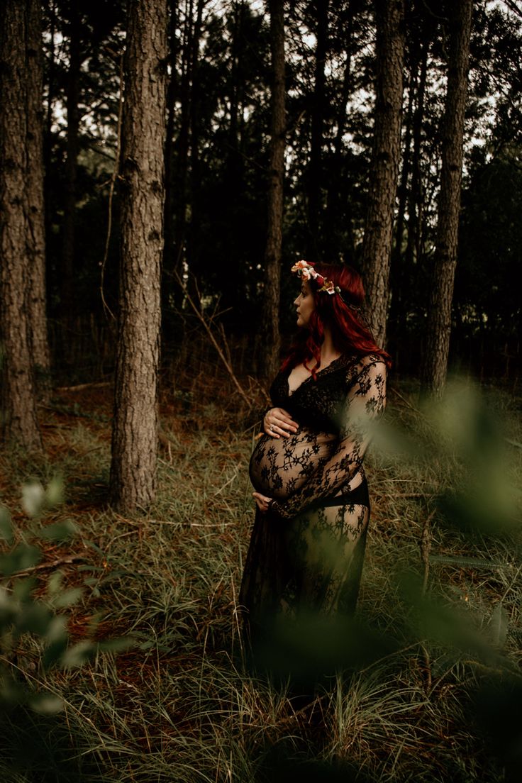 a woman with red hair is standing in the woods, holding her belly up to her chest