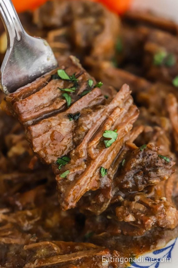 a fork is lifting up some meat from a bowl with carrots and parsley