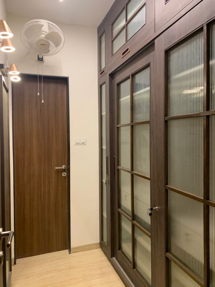 an empty hallway with wooden doors and glass panels on the door, next to a light fixture