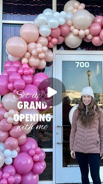 a woman standing in front of a grand opening with pink and white balloons