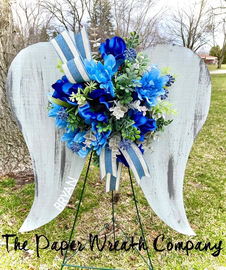 a blue and white flower arrangement on top of an easel in front of a tree