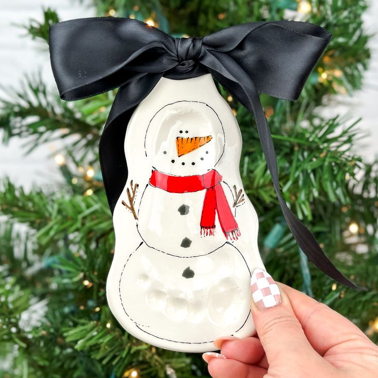 a snowman ornament hanging from a christmas tree with a black ribbon on it