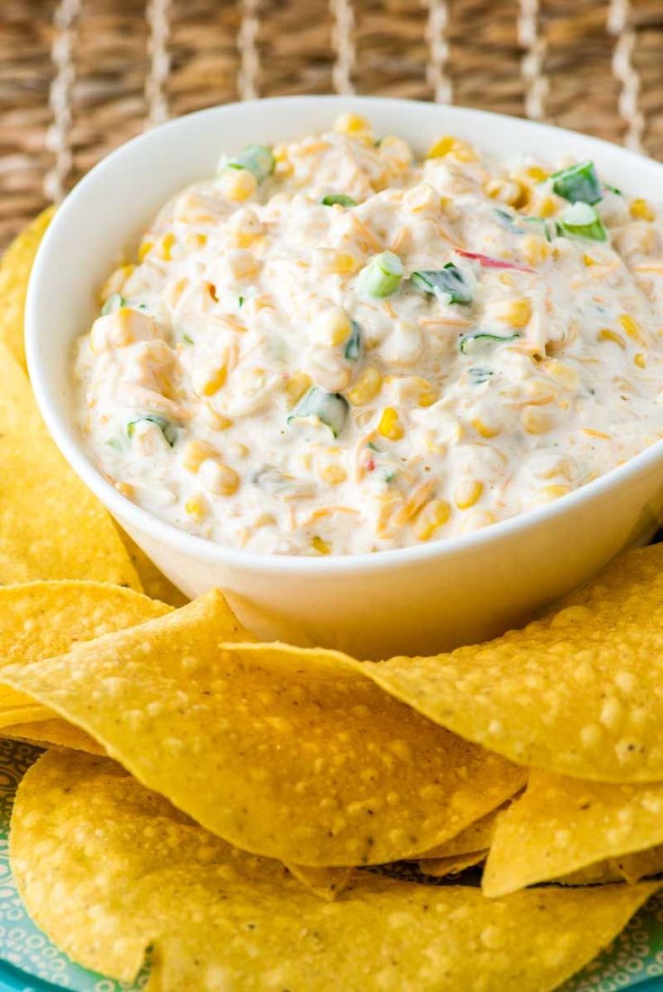 a bowl of white dip surrounded by tortilla chips on a blue and green plate