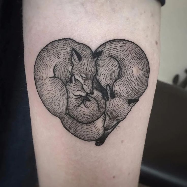 a black and white photo of a heart shaped tattoo on the leg, with two foxes hugging each other