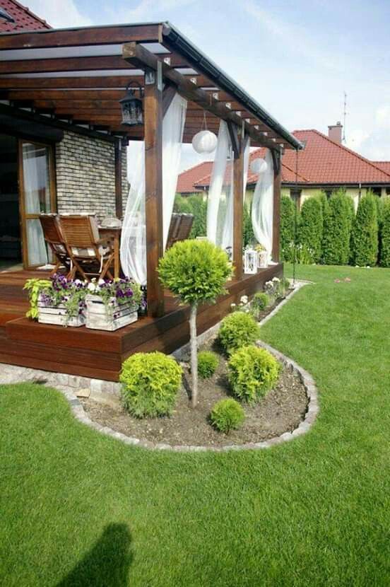 an outdoor covered patio with plants and flowers in the grass, along with a wooden gazebo