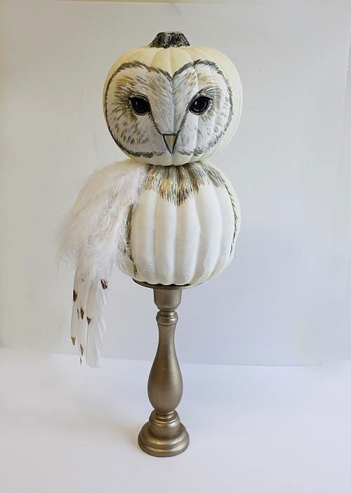 an owl statue sitting on top of a metal stand with feathers around it's eyes