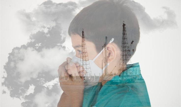 a young man is looking at his cell phone in front of smokestacks and clouds