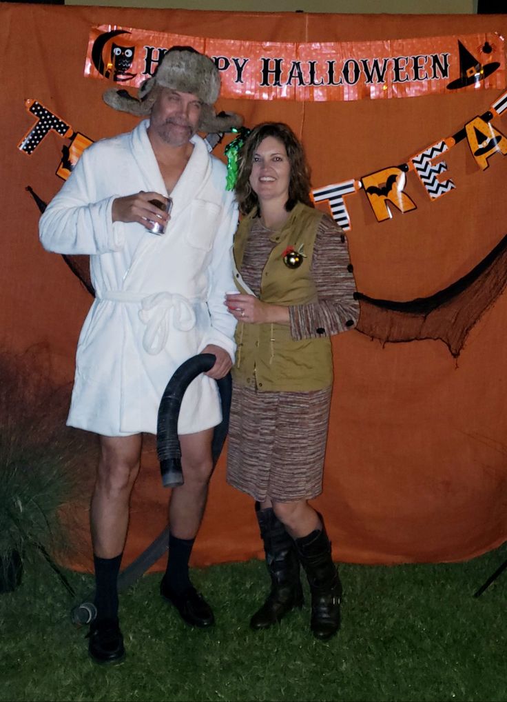 a man and woman dressed up in costumes posing for a photo with an orange banner behind them