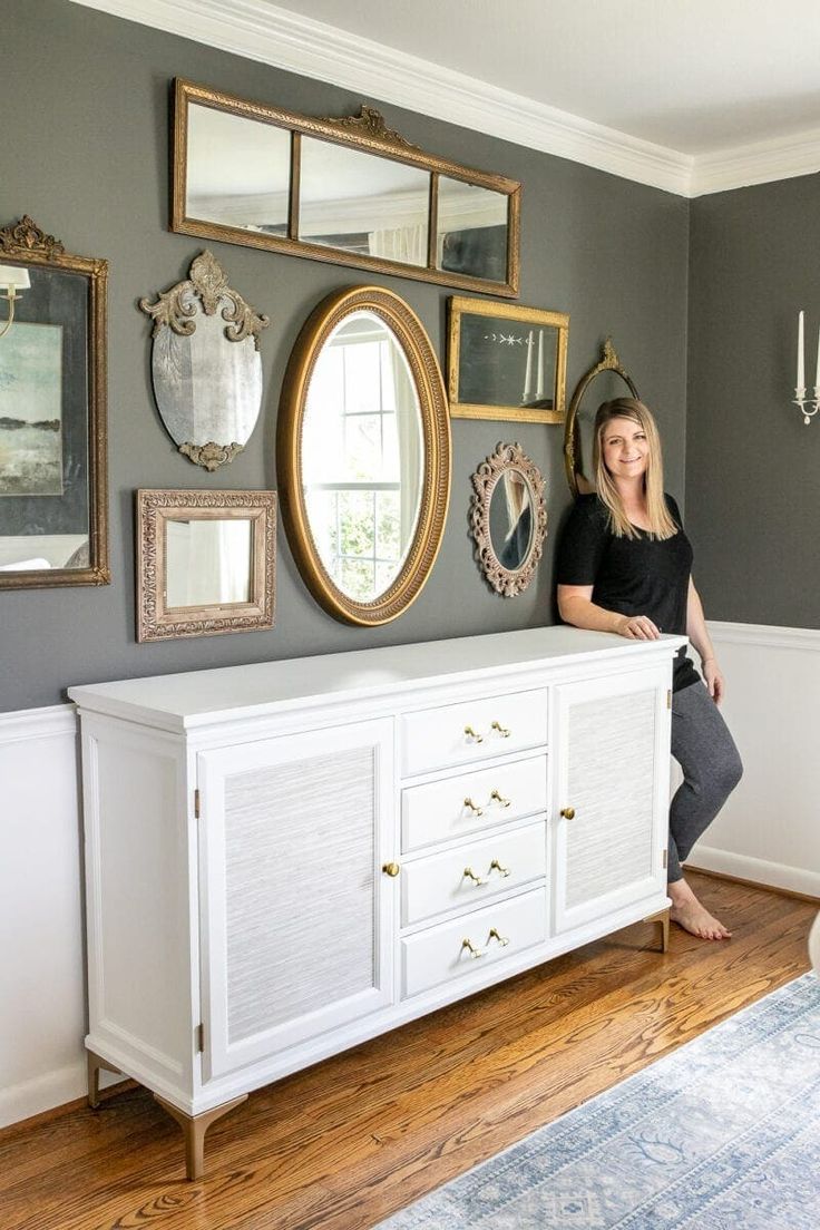 a woman sitting on top of a white dresser next to a wall filled with mirrors