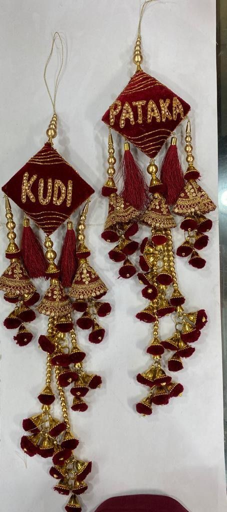 two red and gold earrings hanging from the side of a white wall with writing on it