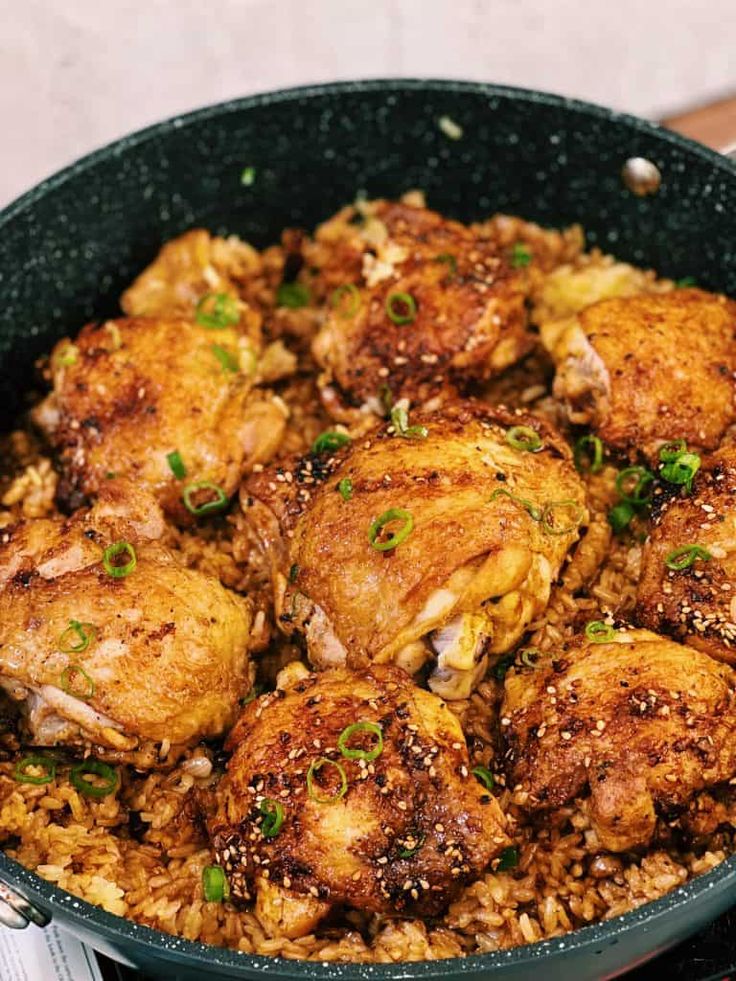 a pan filled with chicken and rice sitting on top of a wooden table next to utensils