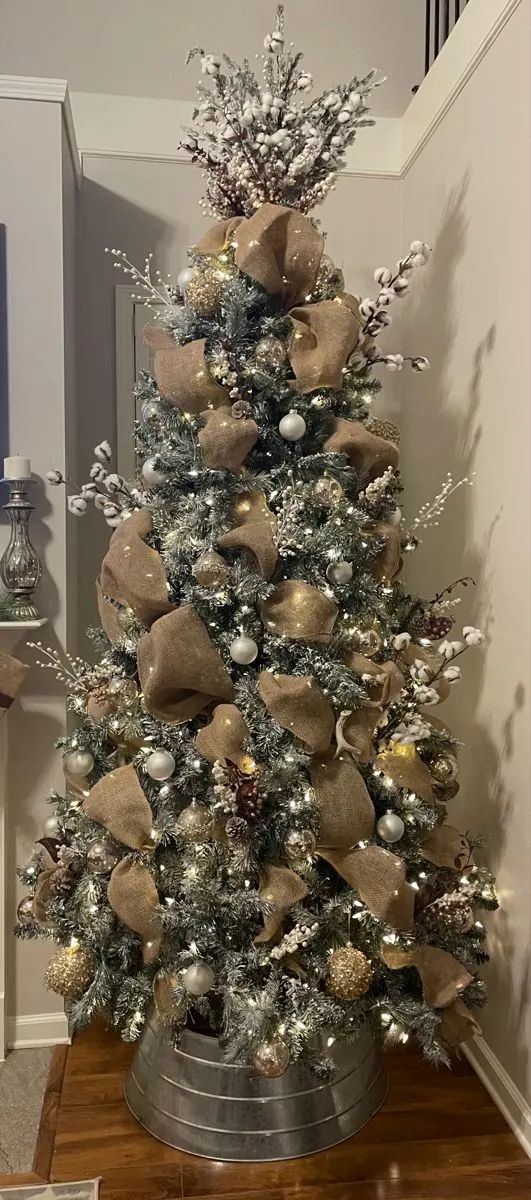 a decorated christmas tree with gold and silver ornaments on it's base, in a living room