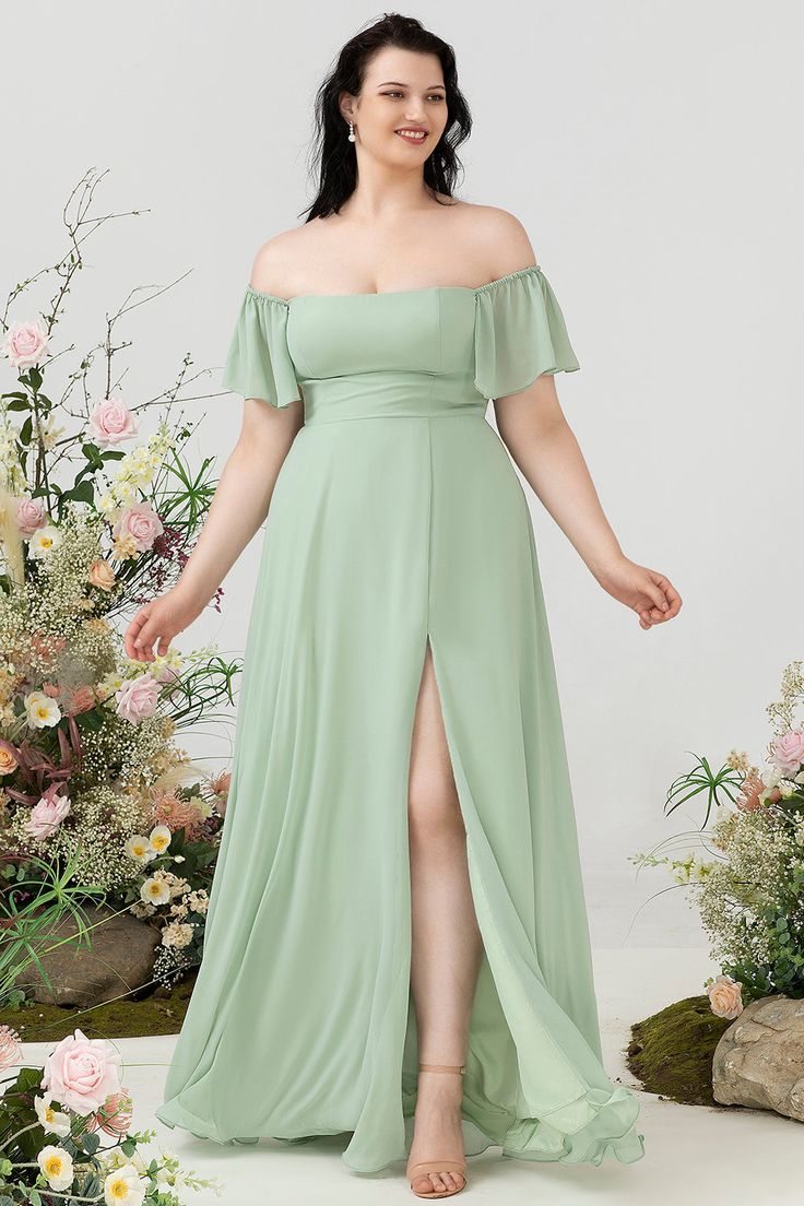 a woman standing in front of flowers wearing a green dress with thigh high slits