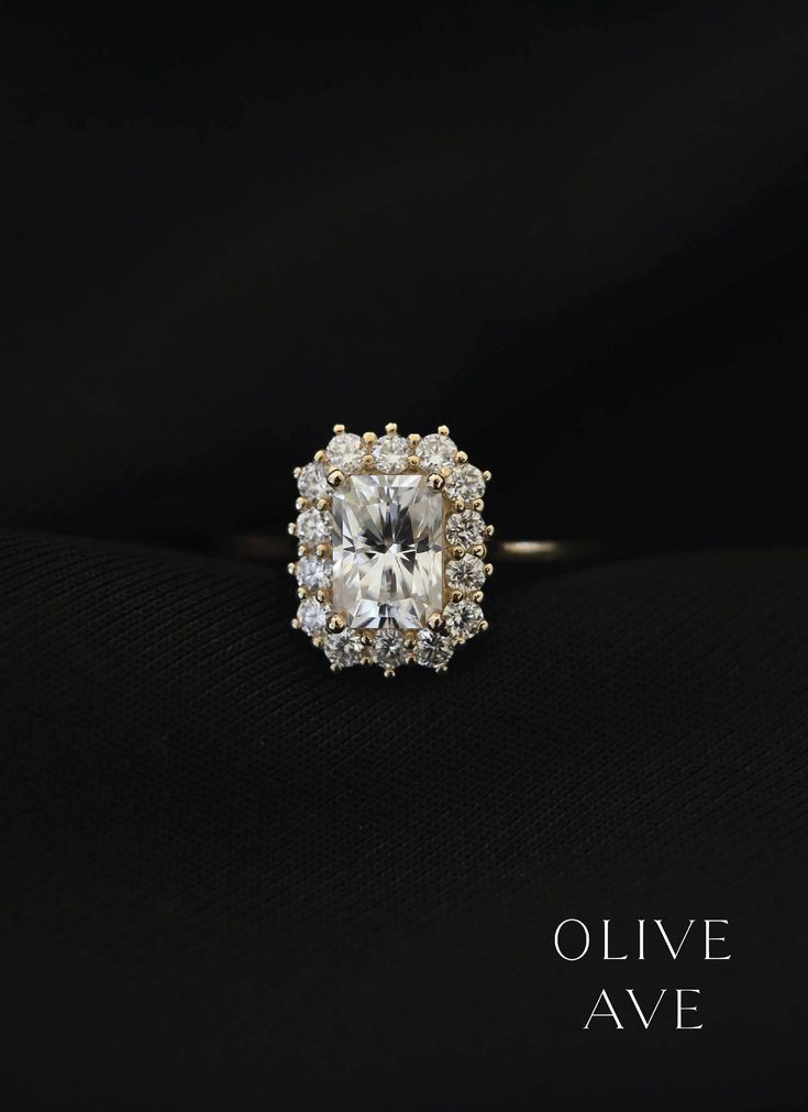 an engagement ring with a cushion cut diamond surrounded by smaller round brilliant diamonds on a black background