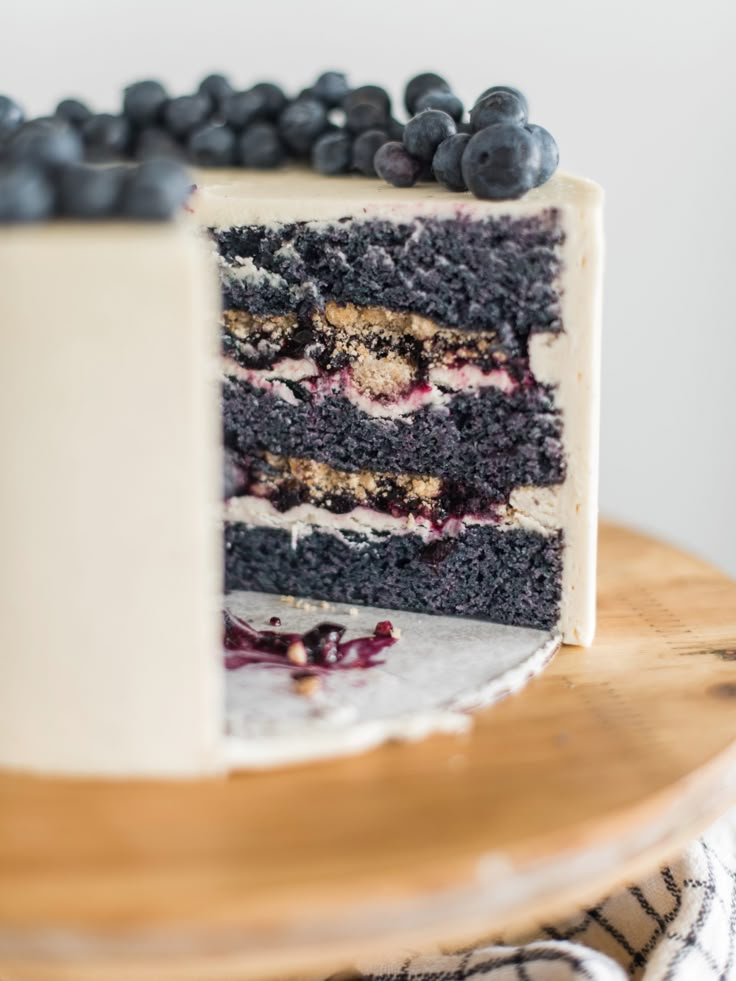 a cake with blueberries and cream frosting is on a wooden platter, ready to be eaten