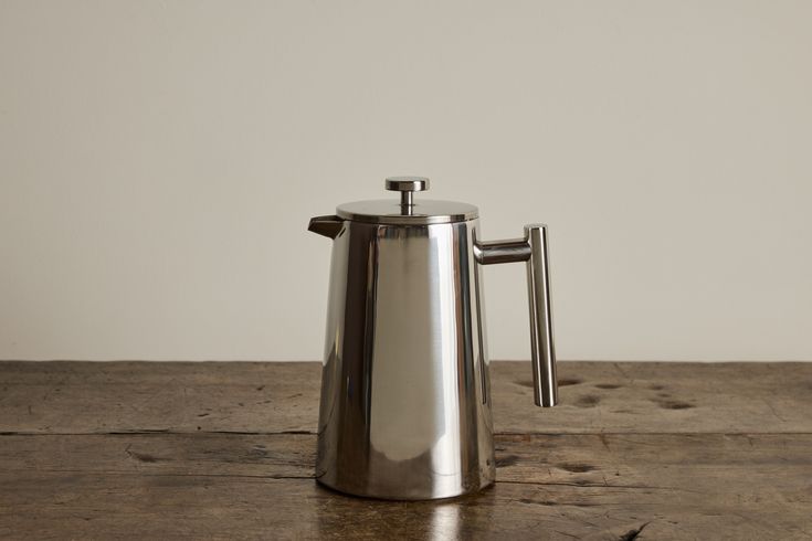 a stainless steel coffee pot sitting on top of a wooden table